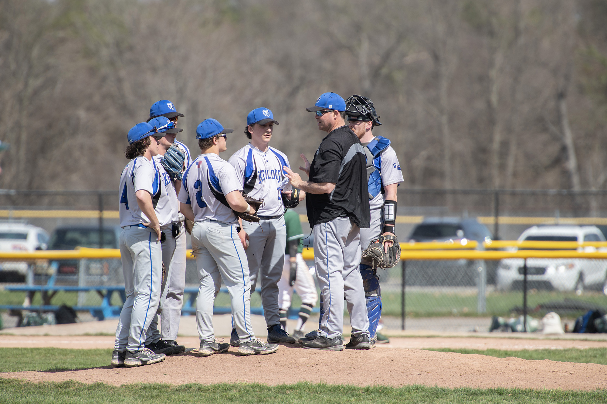 Coach Laskovy meets with players on the pitcher's mound during a game.