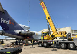 A crane removes a jet engine from the side of an airplane.