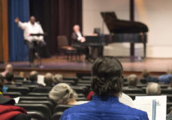 An event attendee sings in the audience area of an auditorium/theater space while facing the stage.