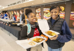 Students pose with takeout containers full of food during a Soul Food Luncheon event on campus.