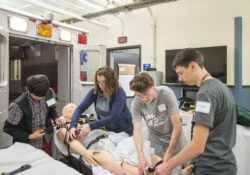 Youth campers prep a manikin on a stretcher to go into an ambulance simulator during and EMS camp.