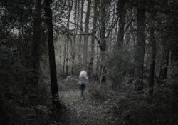 A photograph of a person in the woods. The Best in Show winner titled "Out of the Dark" by Rayna Crane.