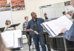 The choir director leads the choir during rehearsal in the choir room.