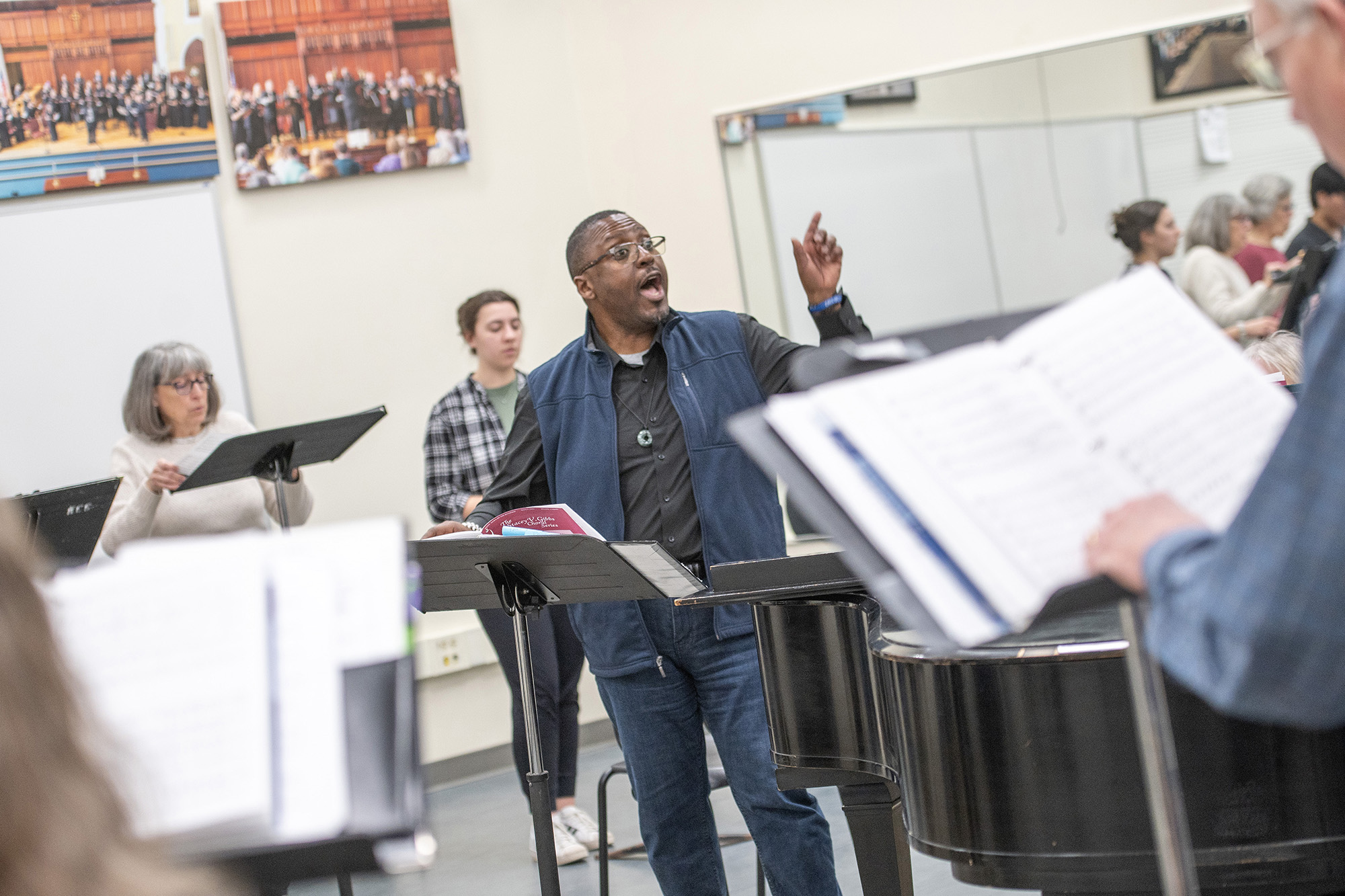 The choir director leads the choir during rehearsal in the choir room.