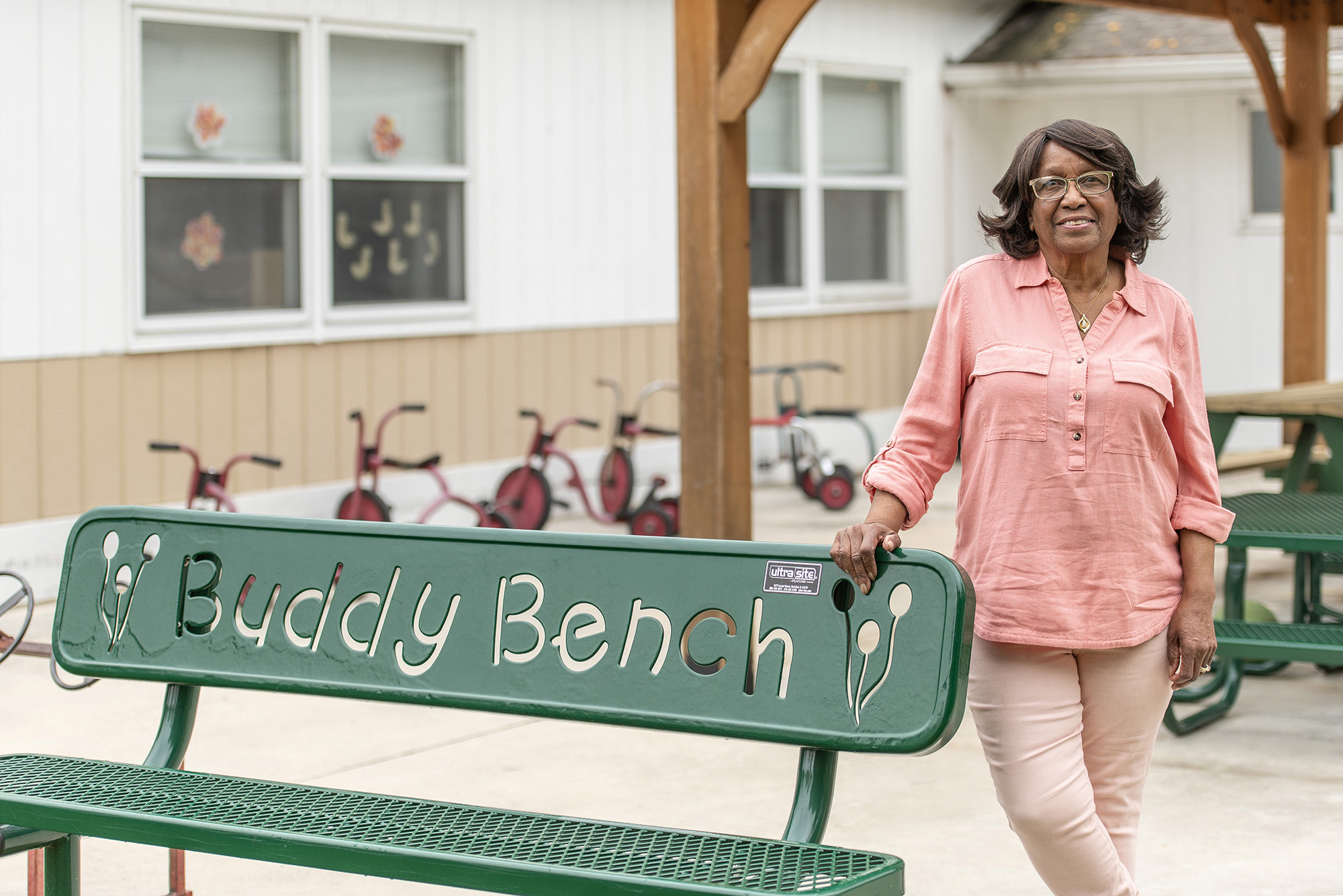 Maude Bristol-Perry stands next to a bench with cutout text on it that reads, "Buddy Bench."