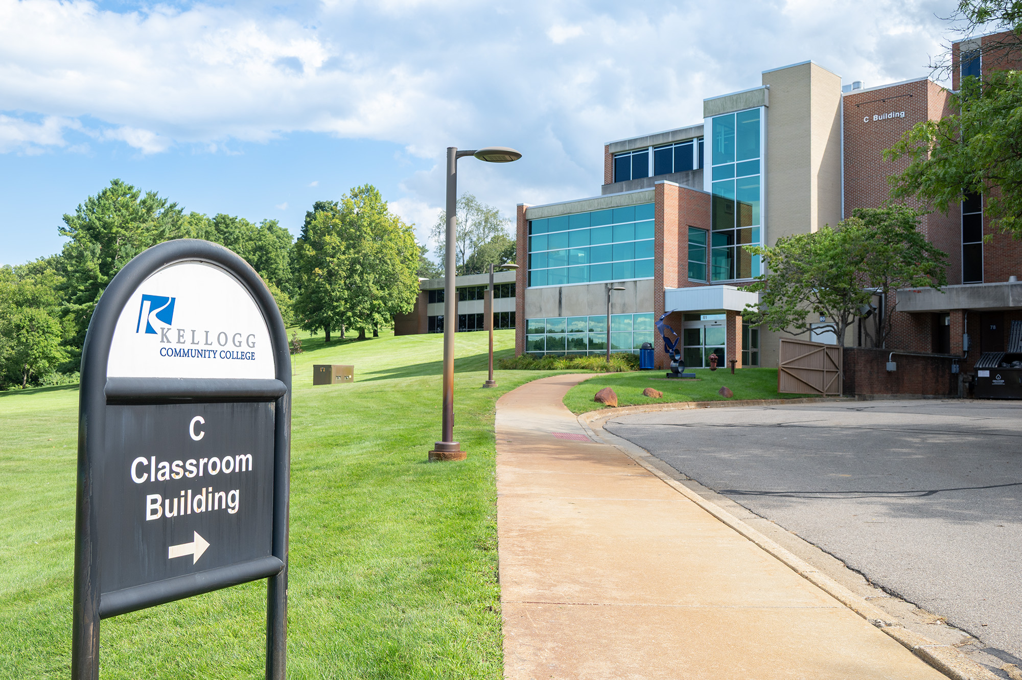 A photo of a sign that reads "C Classroom Building" with an arrow pointing up a walkway to the entrance of the C Building.