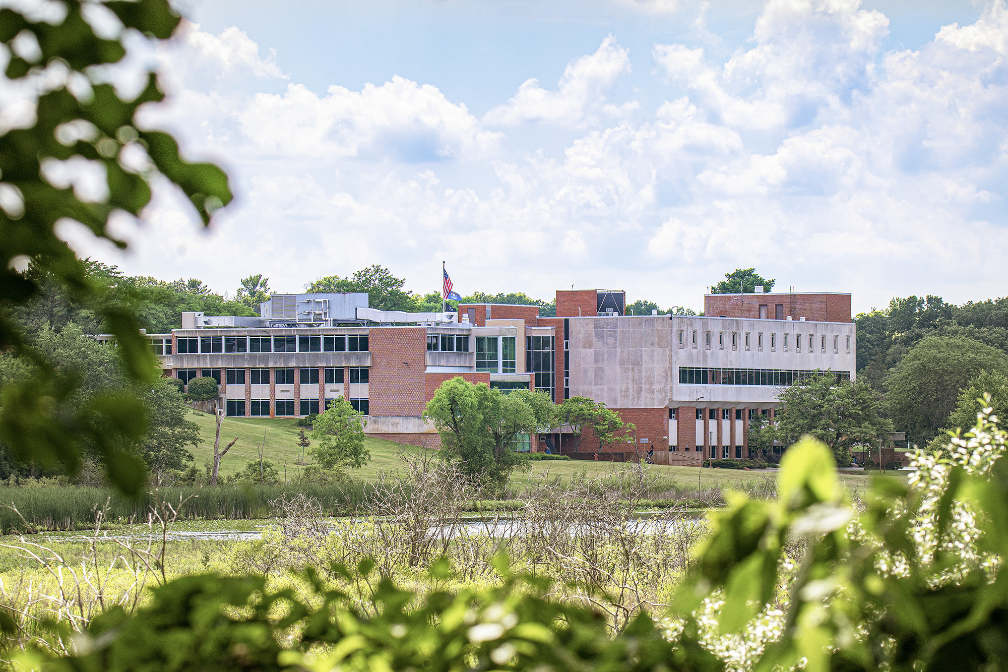A view of buildings on Kellogg Community College's North Avenue campus looking through trees over a lake.