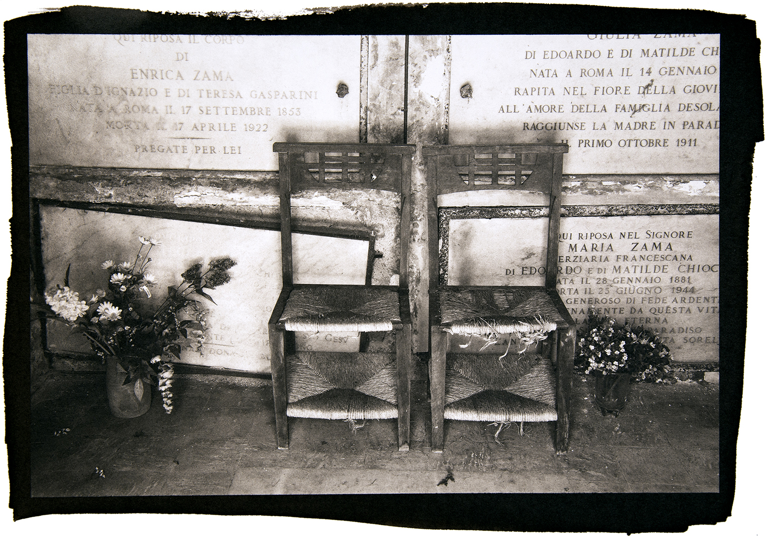 A black and white photo of two empty wooden chairs at a memorial site.